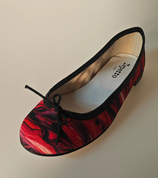 Ballerine imprimée multicolore de Repetto, avec un motif tourbillonnant rouge et noir et un petit nœud décoratif.
