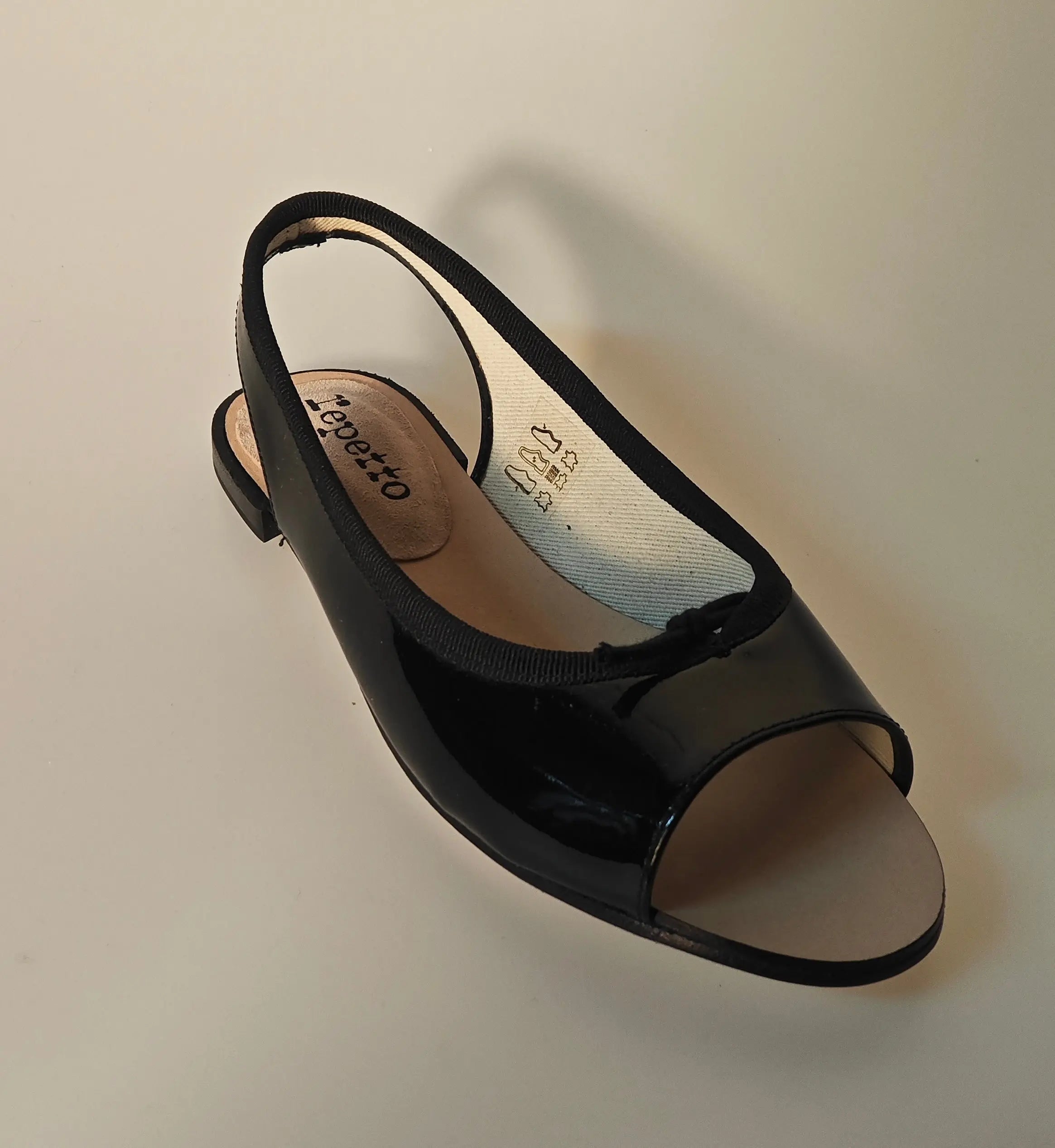 Sandale slingback vernie noire de Repetto, avec bout ouvert et bride arrière.
