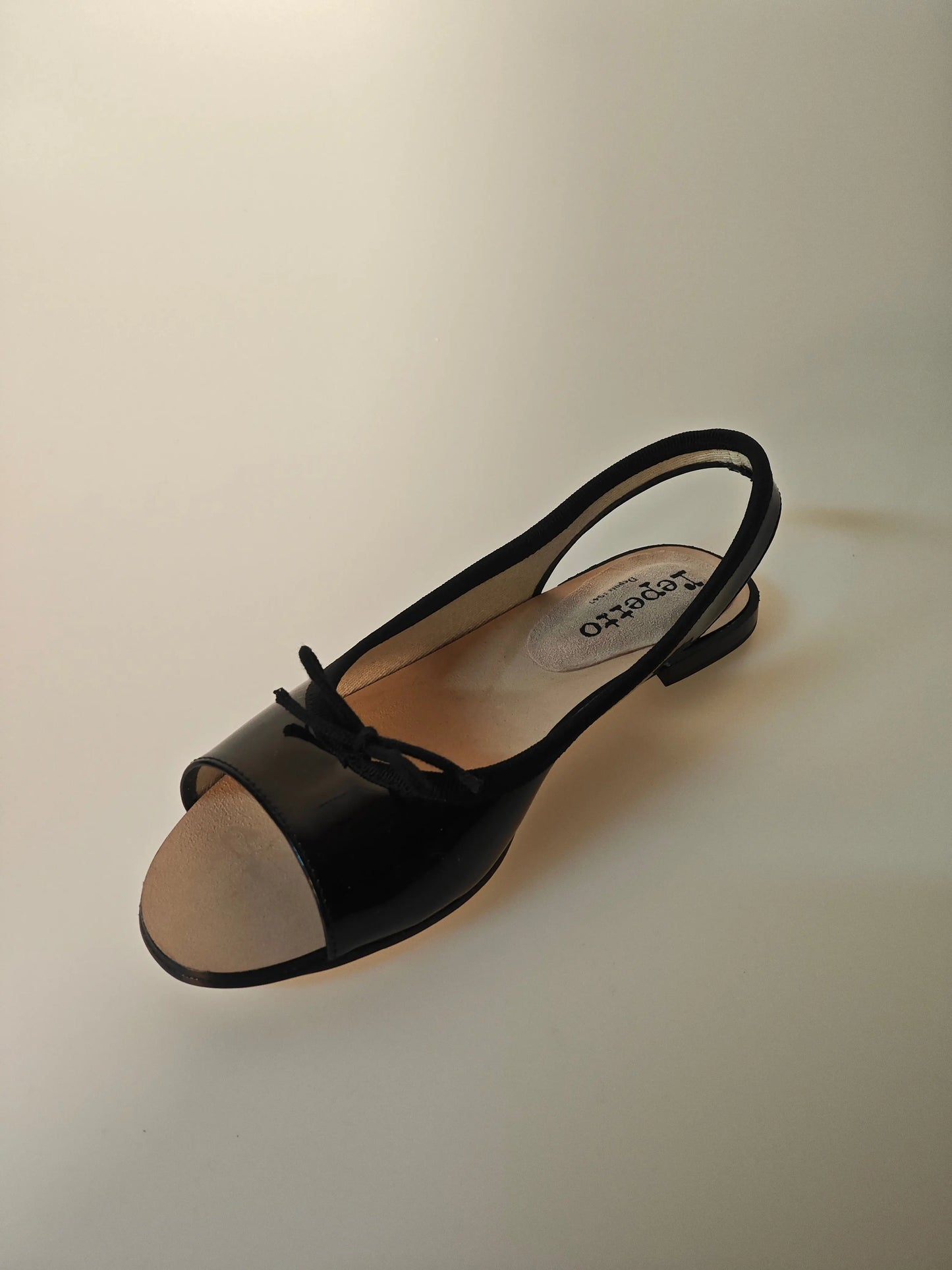 Ballerine slingback vernies noires de Repetto, avec bout ouvert beige et petit nœud décoratif sur le dessus.
