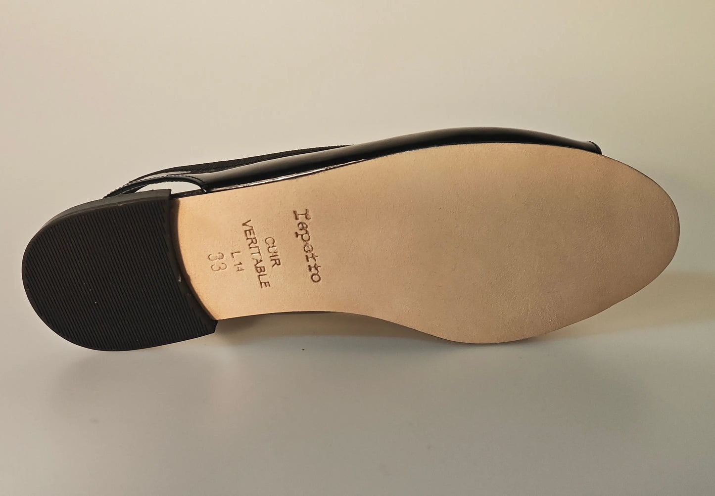 Ballerine slingback vernies noires de Repetto, montrant la semelle en cuir lisse et le talon texturé.
