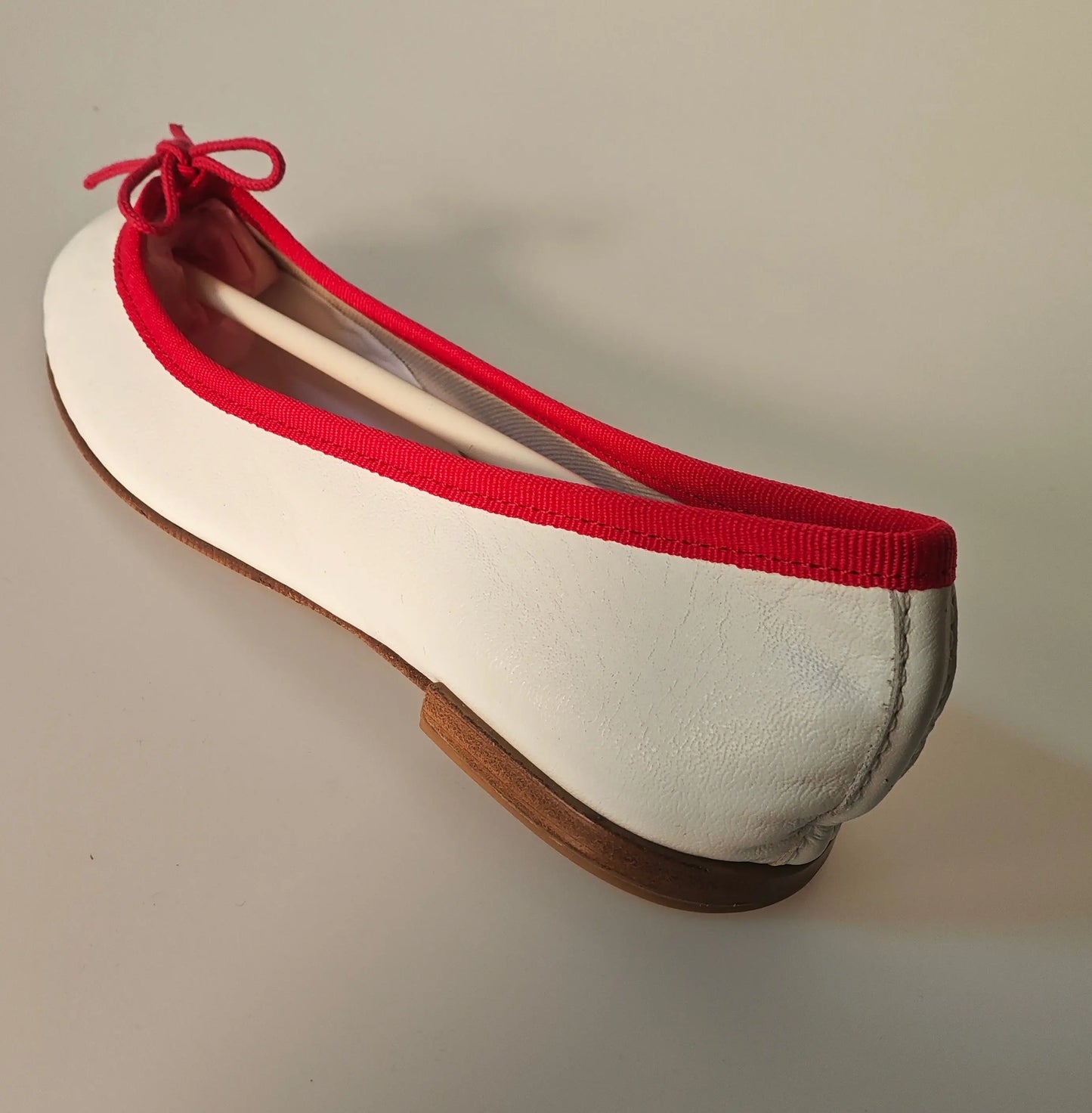 Ballerine Cendrillon en cuir blanc et bordure rouge de Repetto, avec un nœud rouge et une semelle marron.