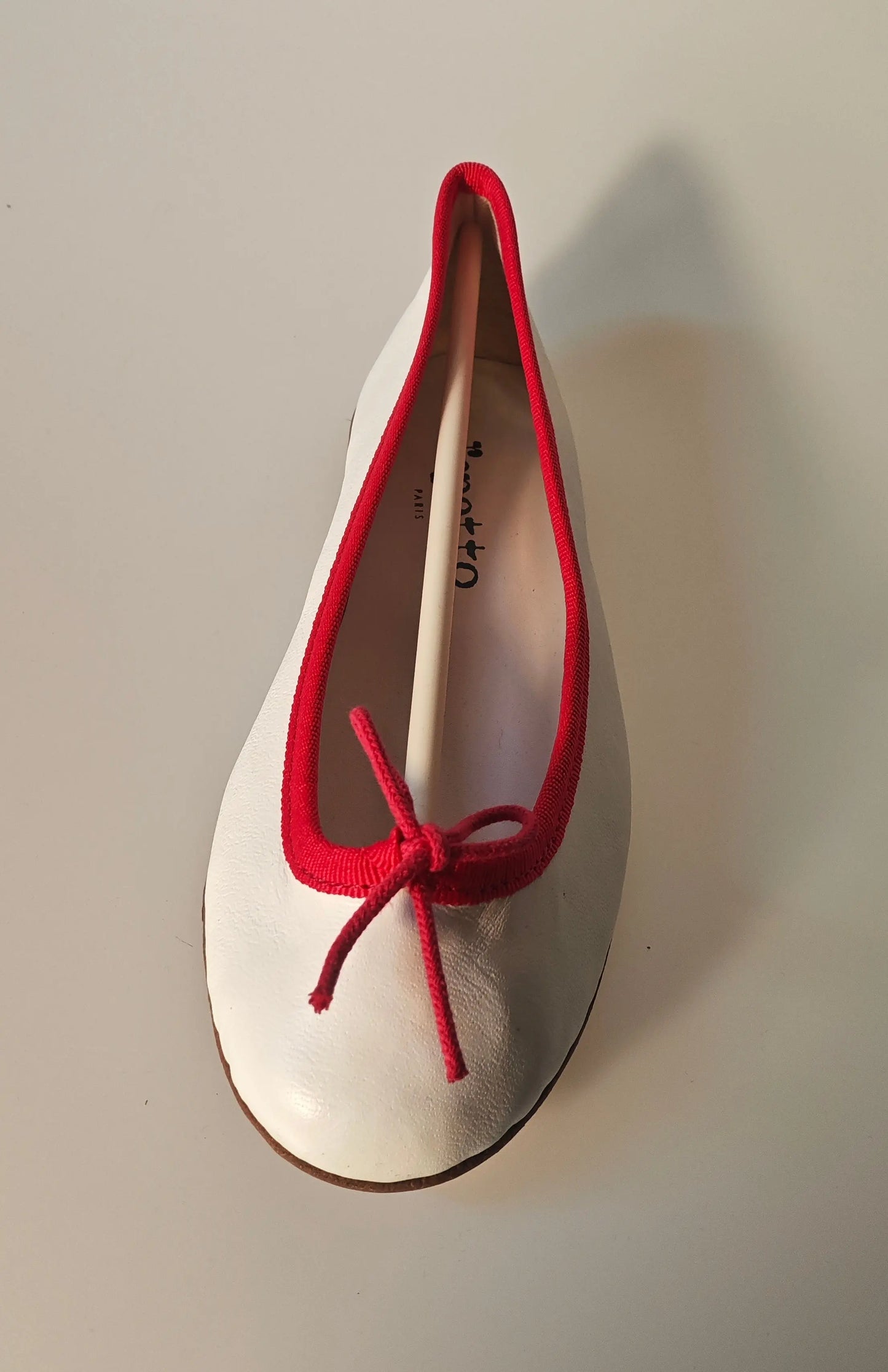 Ballerines blanches en cuir par Repetto, avec bordure rouge et fine bride nouée.