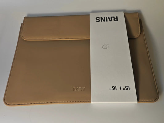 Housse d'ordinateur portable beige de Rains, avec une bande de papier blanche indiquant la taille.
