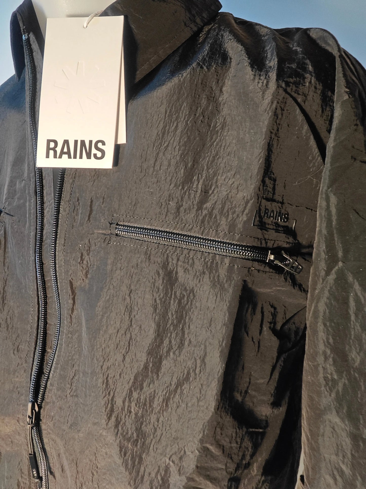 Veste de pluie noire imperméable de Rains, avec fermeture éclair et poche poitrine zippée.