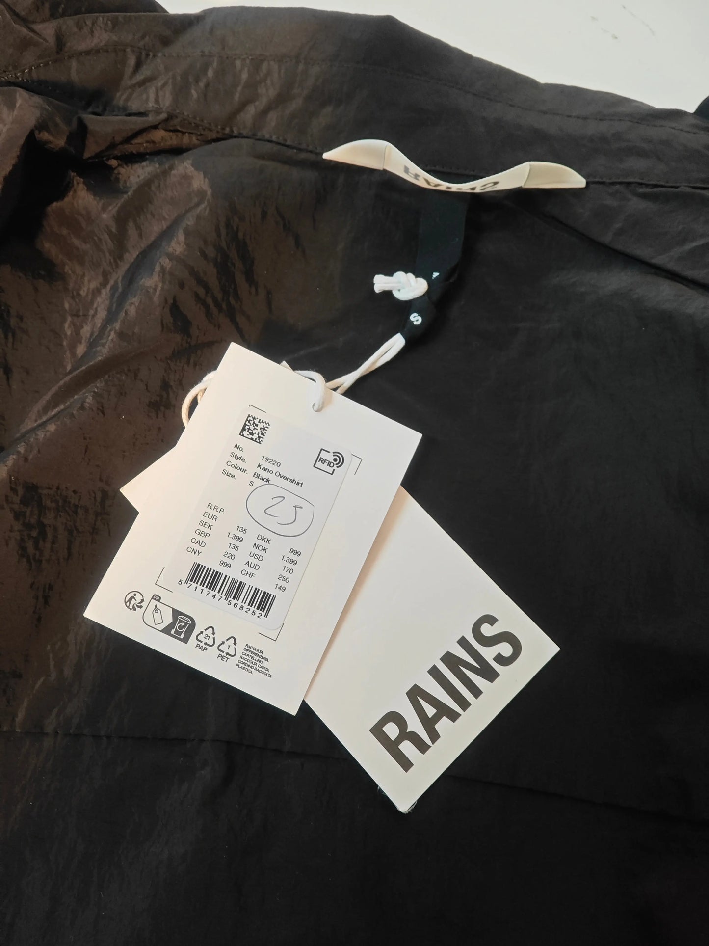 Veste noire imperméable de Rains, avec étiquettes attachées et cordon de serrage à l'encolure.
