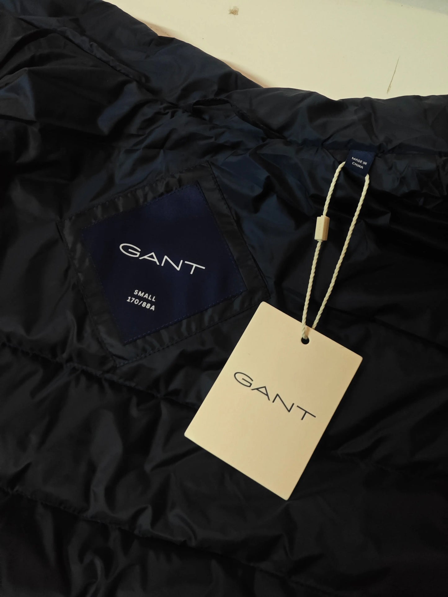 Doudoune sans manches bleu marine de Gant, avec étiquette cartonnée beige et indication de taille.