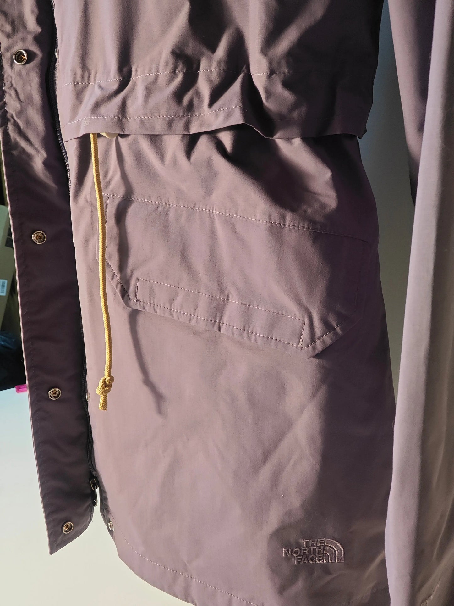 Parka violet lavande pour femme de The North Face avec capuche, poche et cordon jaune.