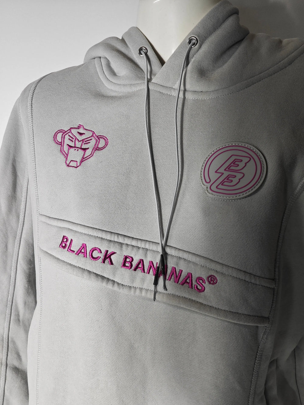 Hoodie gris clair de Black Bananas® avec logo rose et détails décoratifs, présenté sur un mannequin.