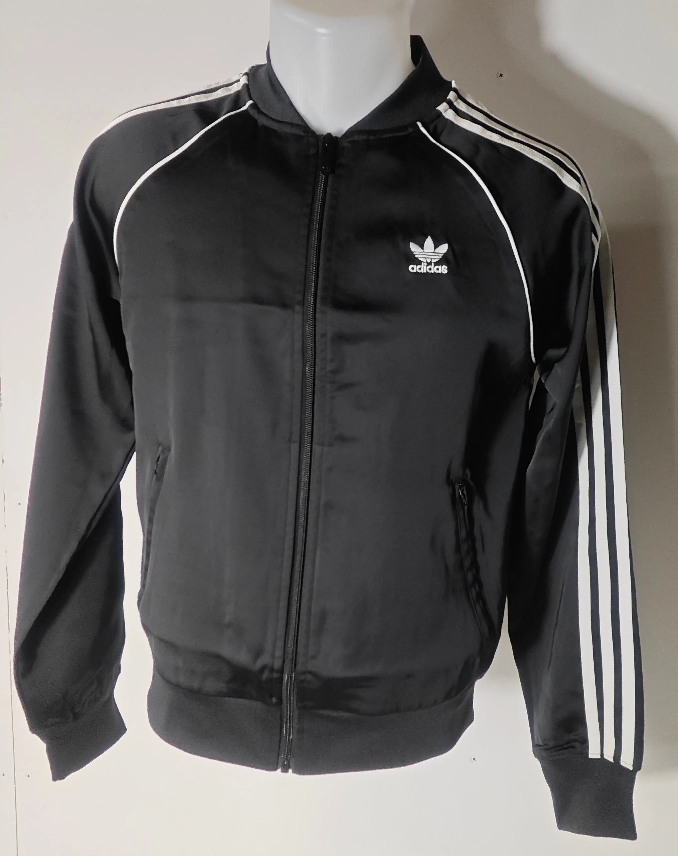 Veste noire en satin d'Adidas Originals, avec les trois bandes blanches emblématiques sur les manches.