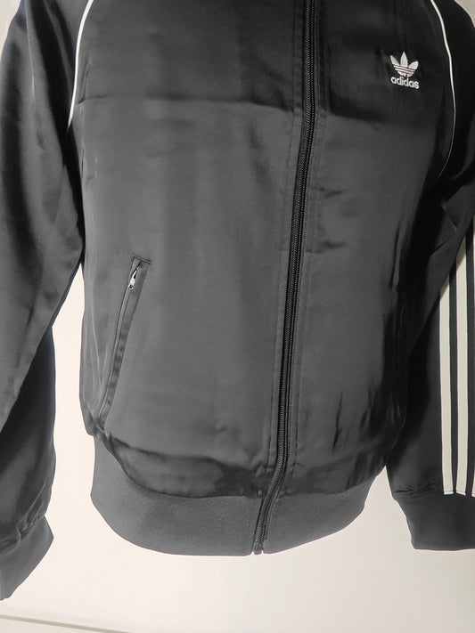 Veste de survêtement noire satinée, par Adidas, avec fermeture éclair et bandes blanches distinctives sur les manches.