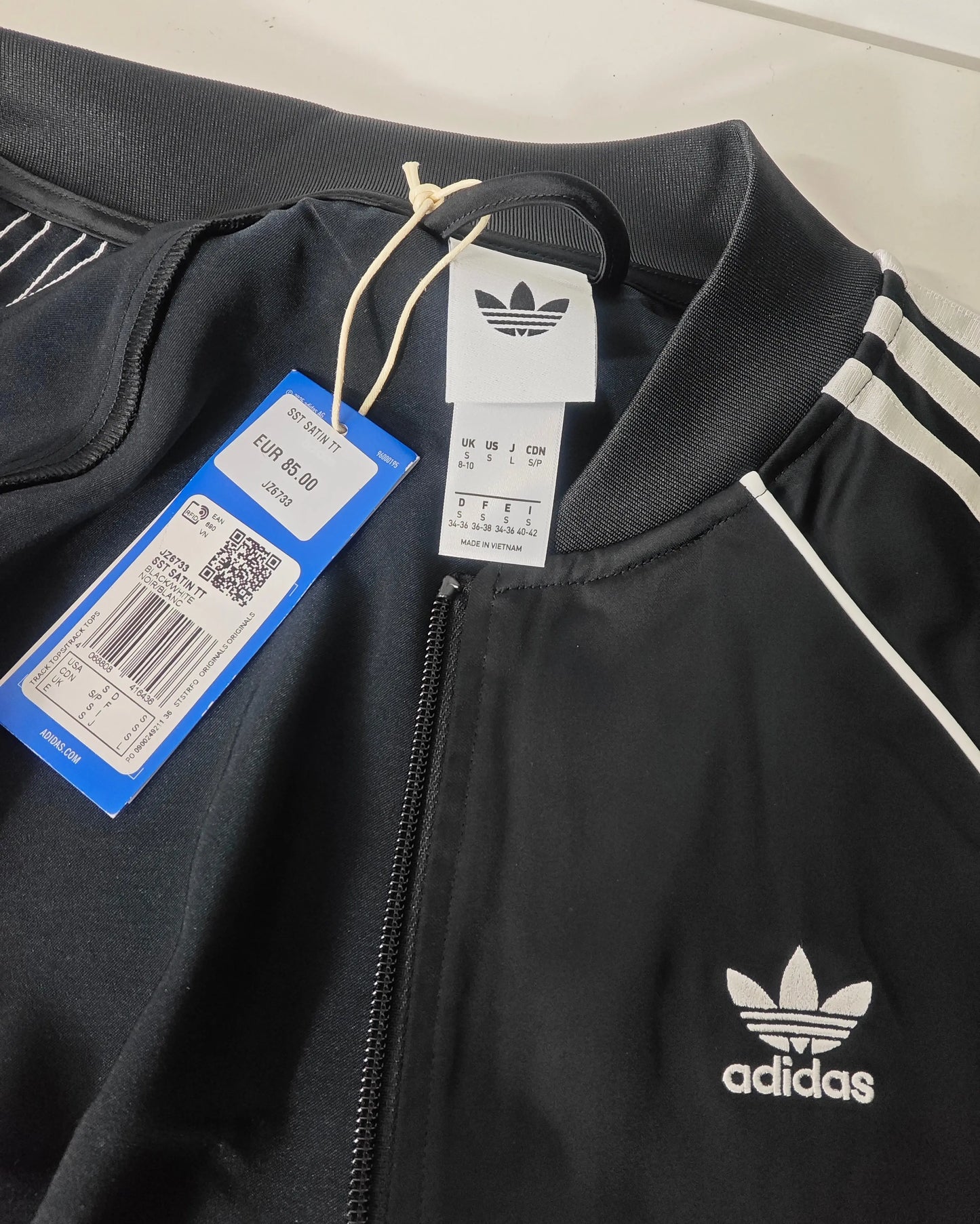 Veste de survêtement SST en satin noir d'Adidas Originals, avec fermeture éclair et les trois bandes blanches iconiques.
