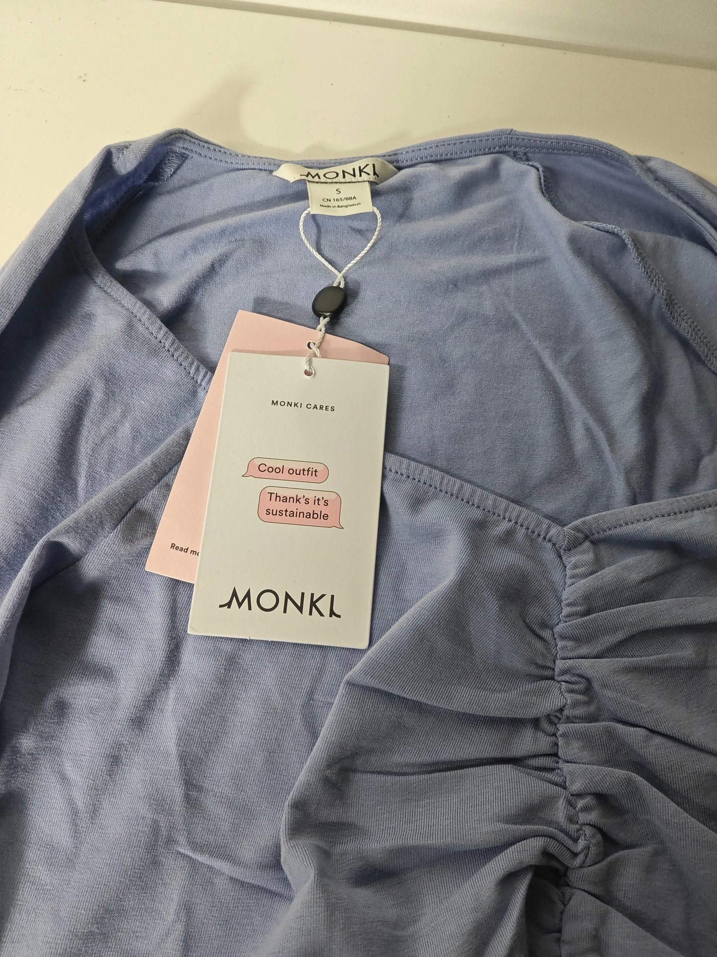 Haut bleu en jersey de Monki, avec détail froncé et étiquette de la marque.
