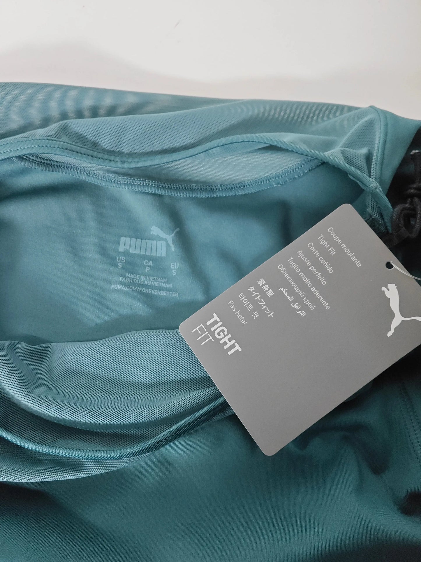 Crop top de sport à manches longues bleu turquoise par Puma, avec étiquette « Tight Fit ».
