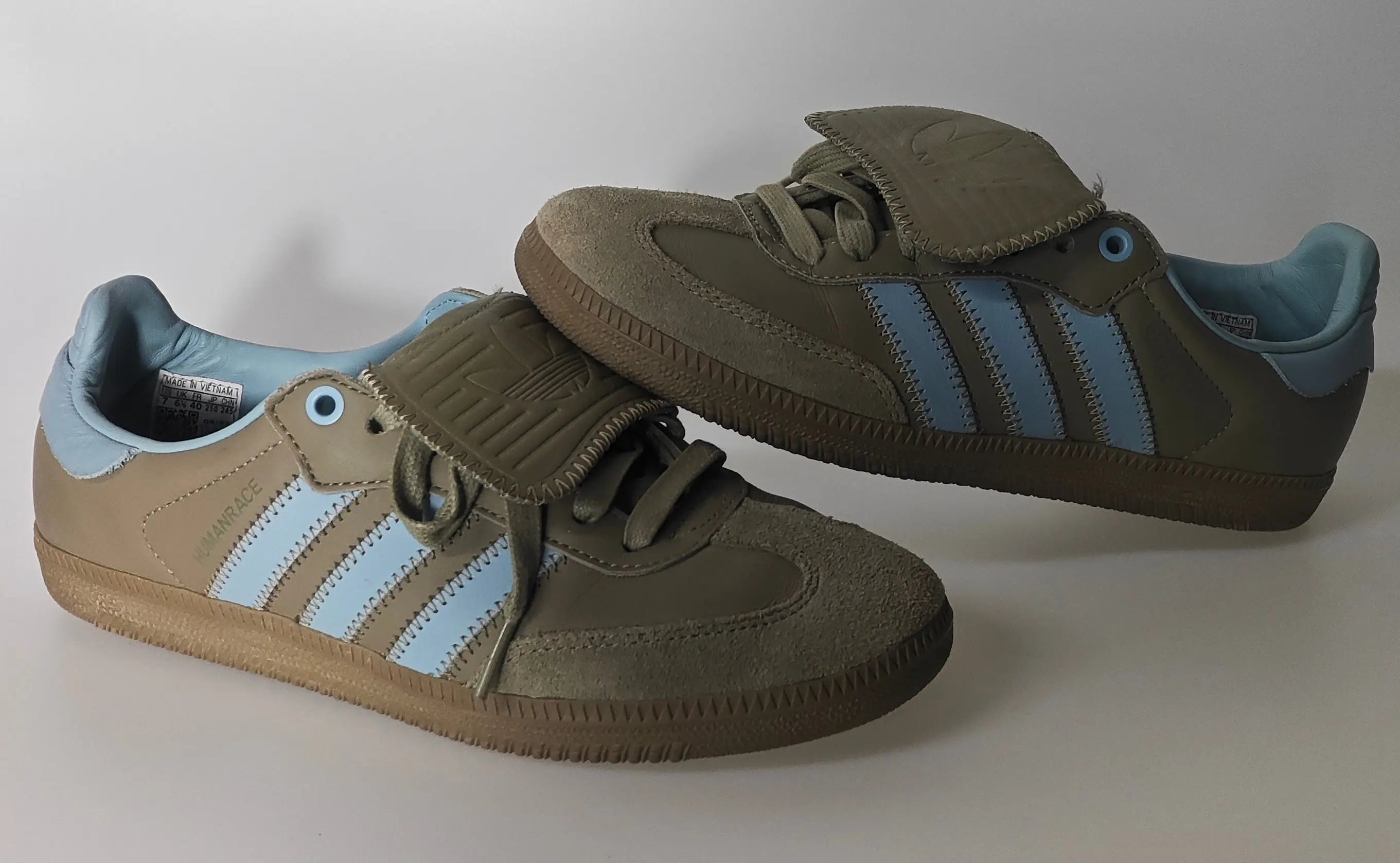 Baskets Samba Humanrace kaki, d'occasion, par Adidas, avec trois rayures latérales bleu ciel et languette recouvrant les lacets.
