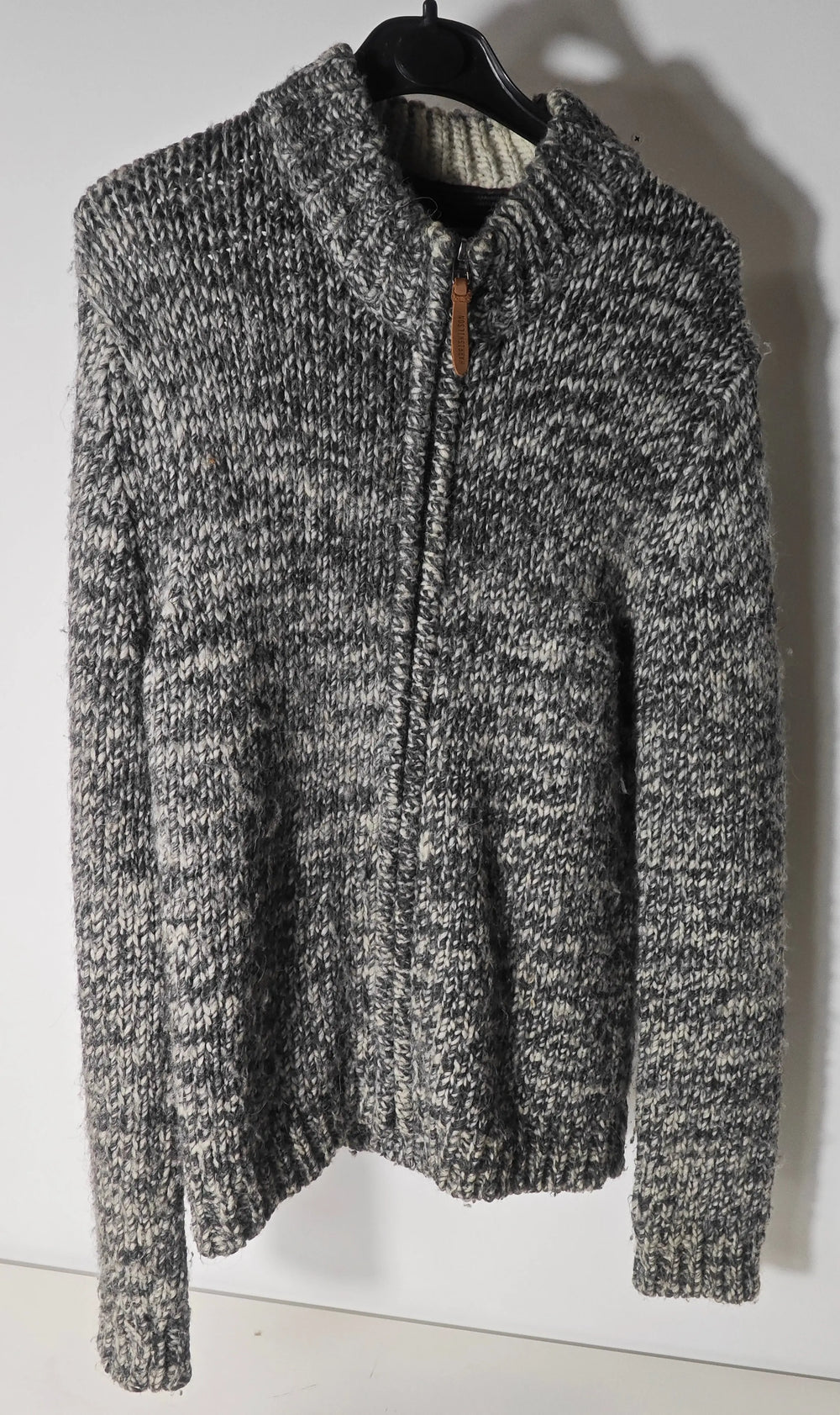 Gilet zippé en laine épaisse gris chiné de Harris Wilson, sur un cintre noir.
