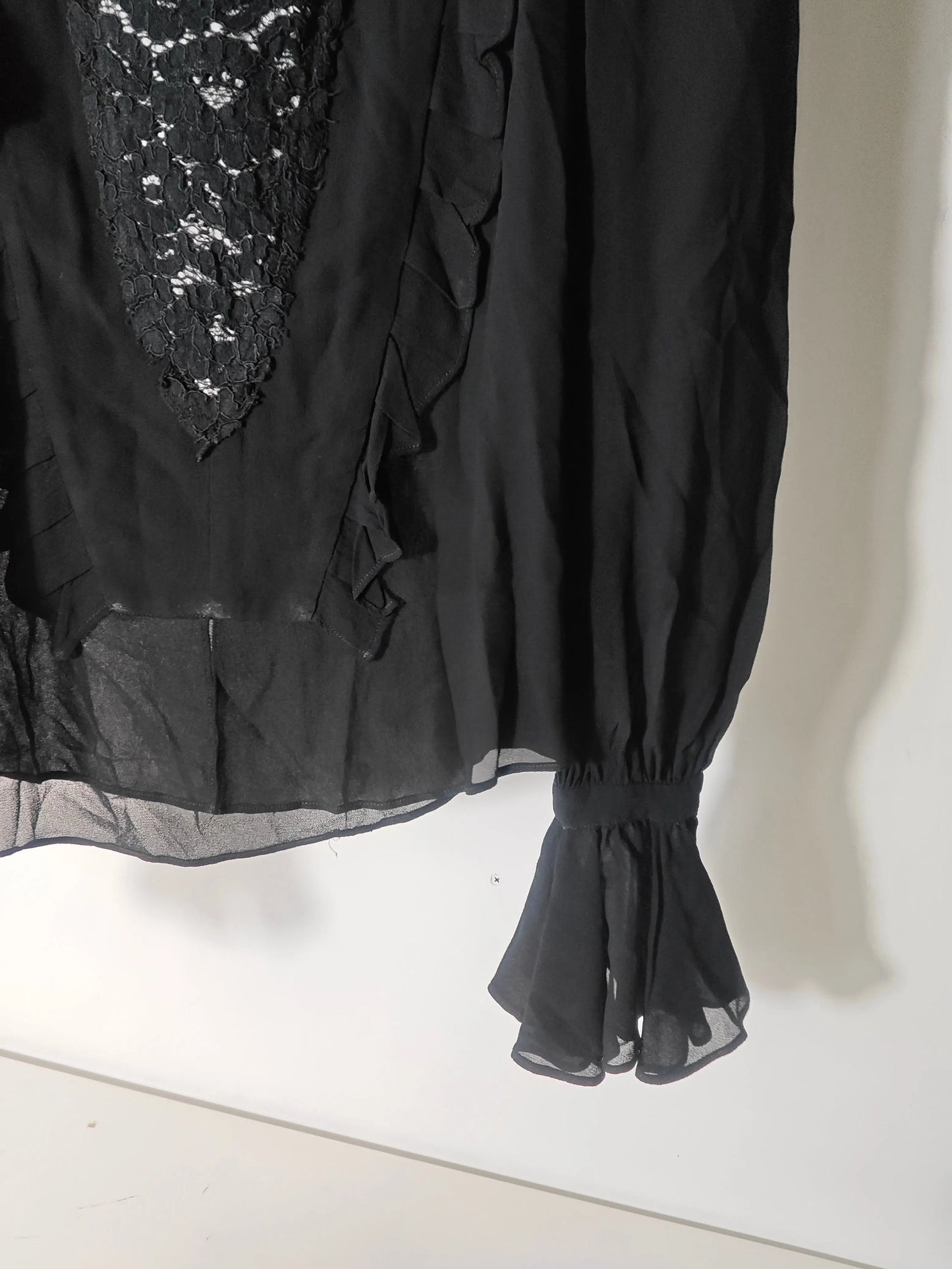 Blouse noire de Belair en dentelle avec volants, manches longues et ourlet transparent.
