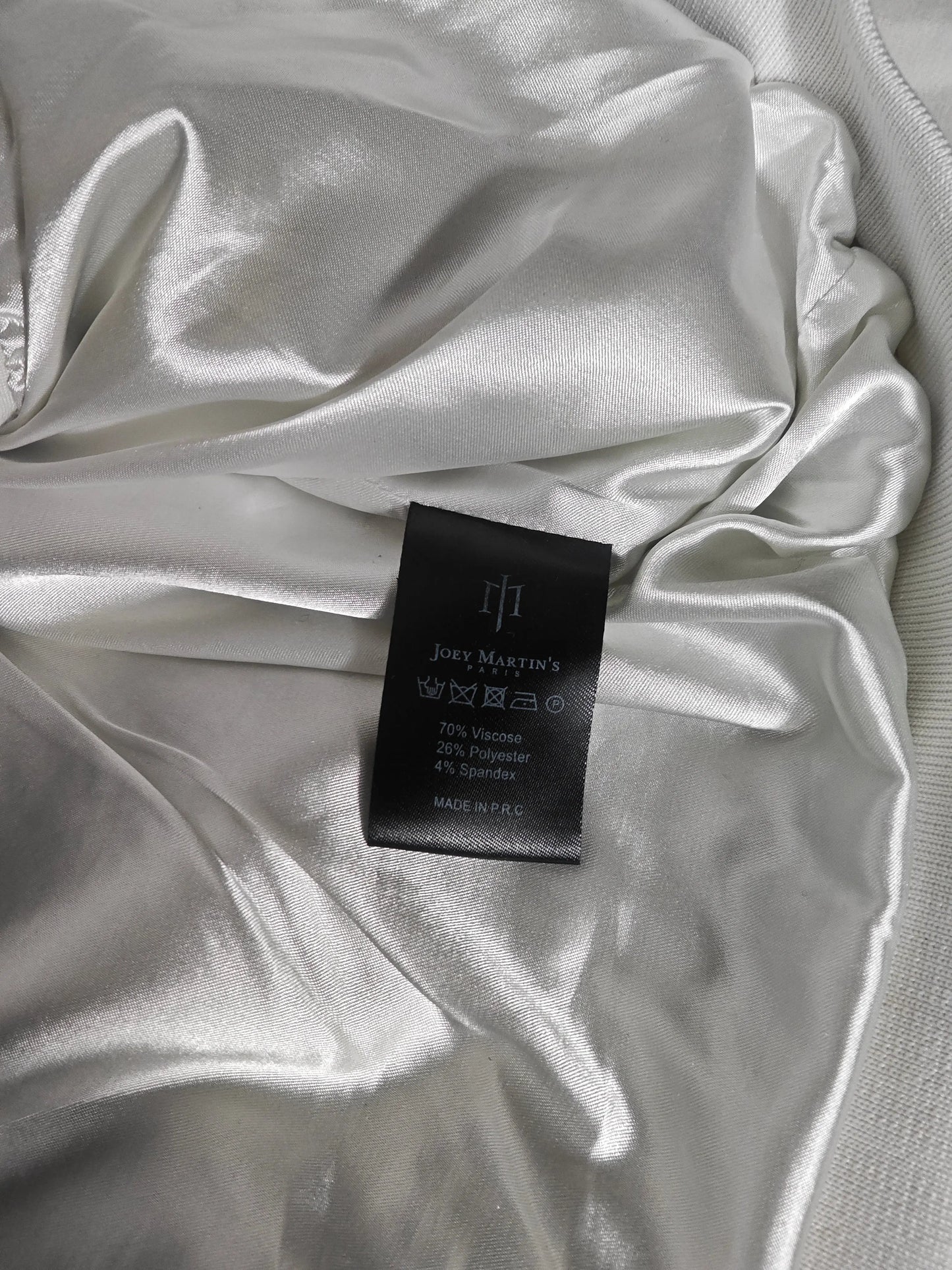 Étiquette de composition d'une veste à capuche blanche de Joey Martin's Paris, avec une doublure brillante et froissée.