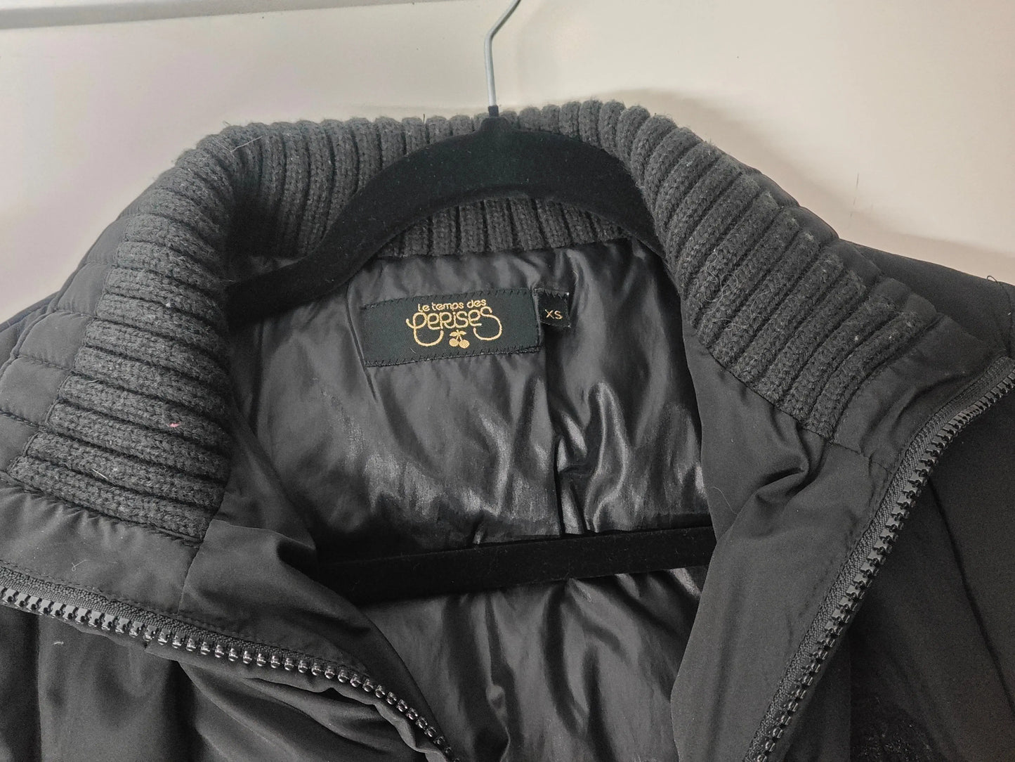 Doudoune noire de Le Temps des Cerises avec col en tricot côtelé sur un cintre.