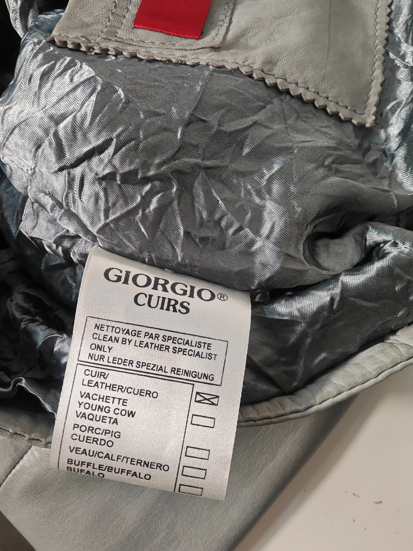 Veste en cuir gris, de Giorgio & Mario, avec étiquette d'entretien visible.
