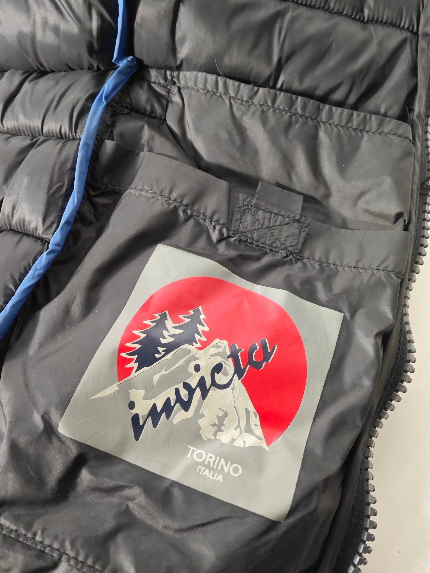 Doudoune noire par Invicta, avec logo montagne rouge et gris sur la poche intérieure.