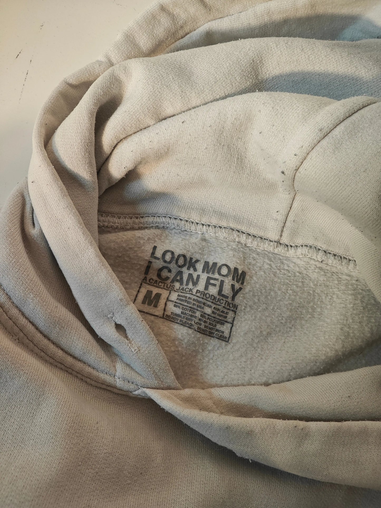 Sweat à capuche beige d'occasion par Travis Scott, avec étiquette 'Look Mom I Can Fly' et cordon.