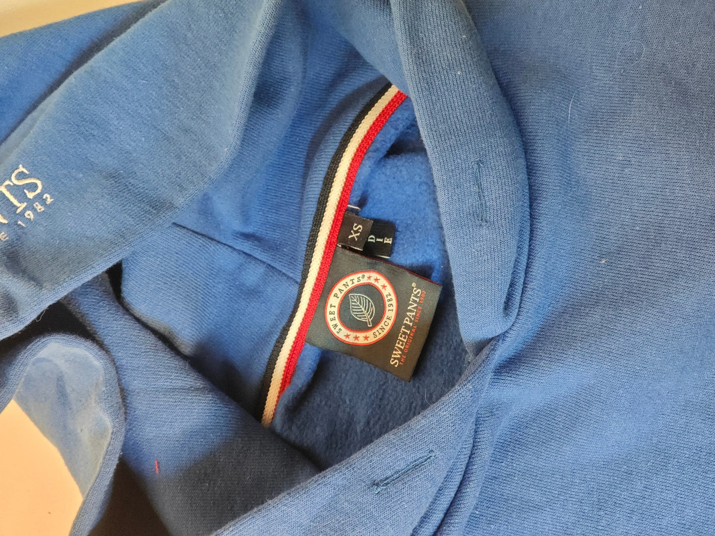 Sweat à capuche bleu oversize de Sweet Pants, avec des détails tricolores et une étiquette de taille XS.
