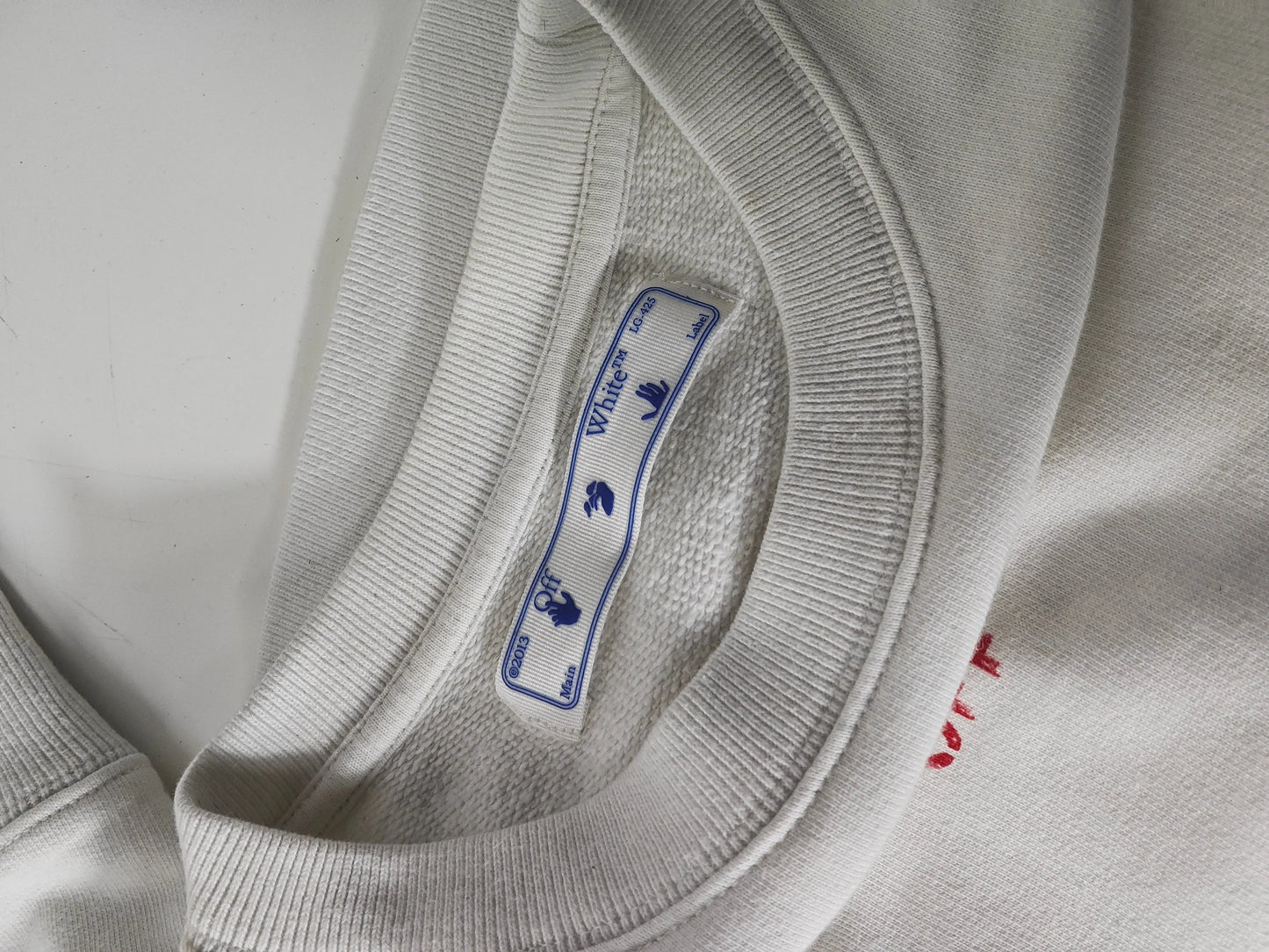 Sweat-shirt blanc à motif flèches rouges de Off-White™, détail du col et de l'étiquette de la marque.