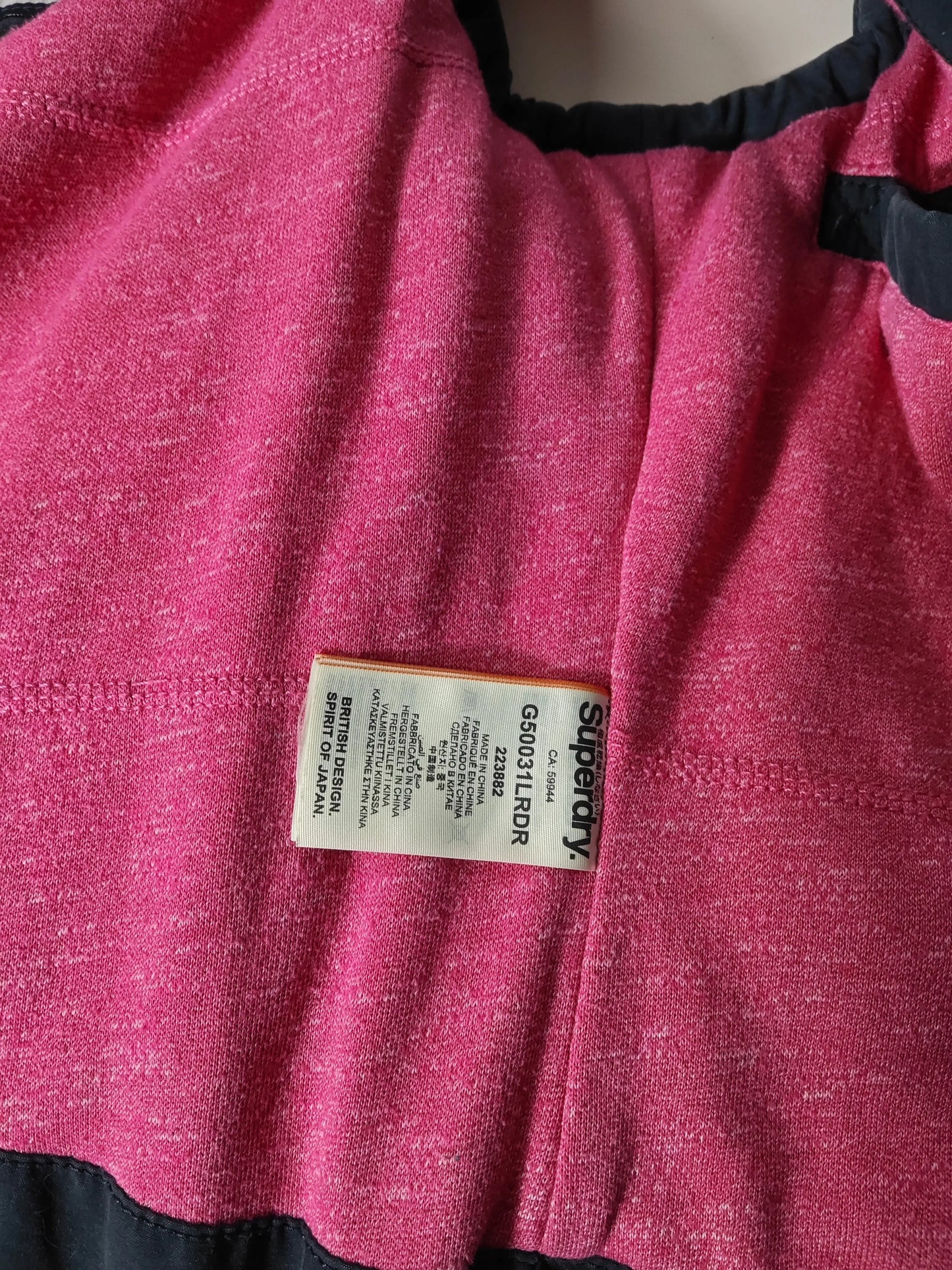 Doudoune sans manches rose chiné de Superdry avec étiquettes de composition apparentes.
