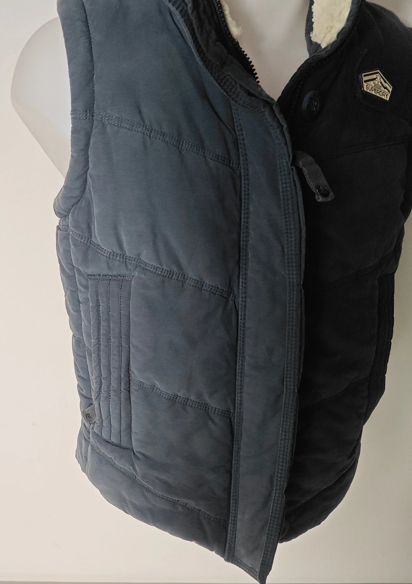 Doudoune sans manches bleue de Superdry avec col en fausse fourrure, motif matelassé.
