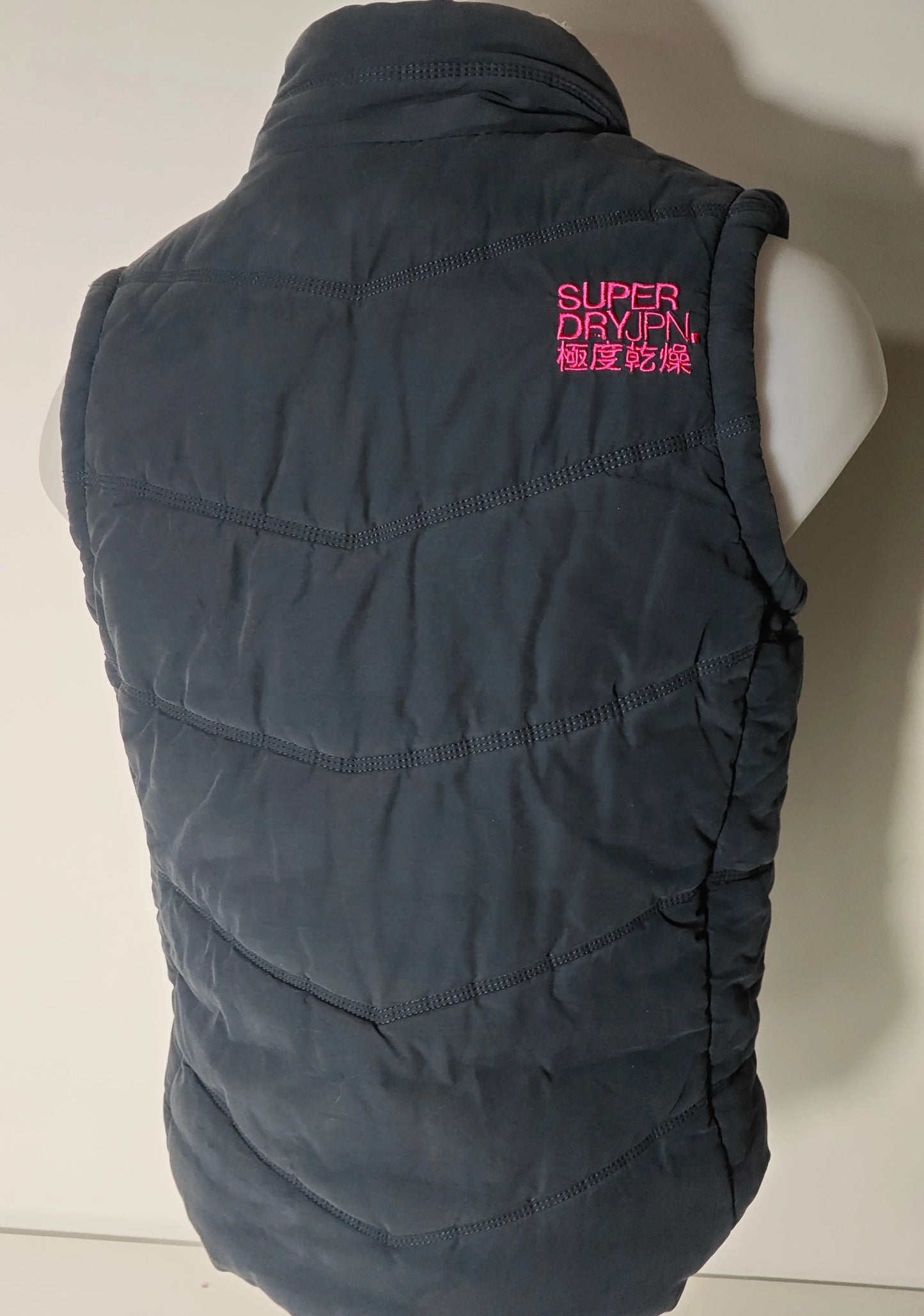 Doudoune sans manches noire de Superdry avec surpiqûres horizontales et logo rose.
