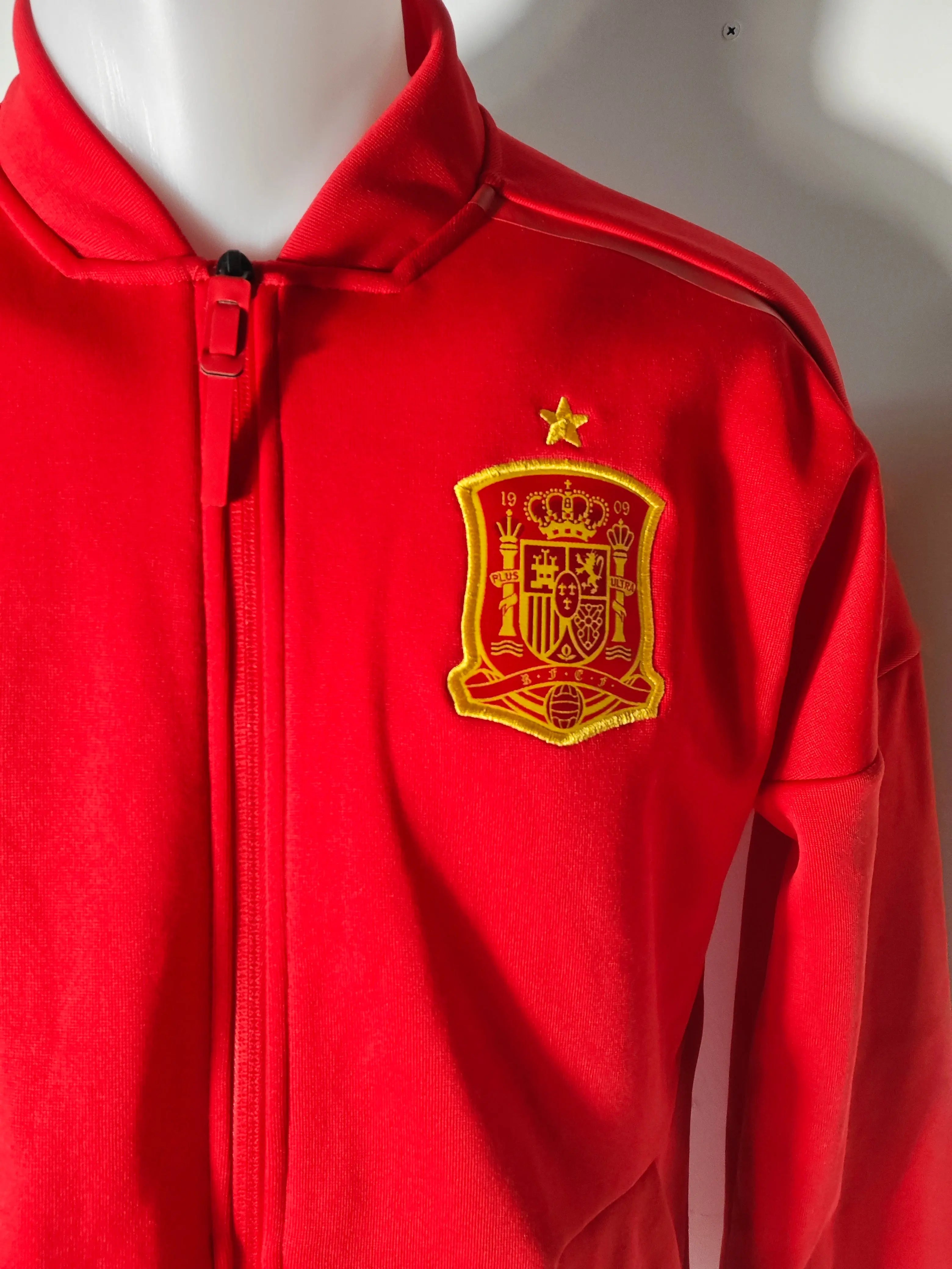 Veste de survêtement rouge et jaune par Adidas, avec l'écusson de l'Espagne sur la poitrine.