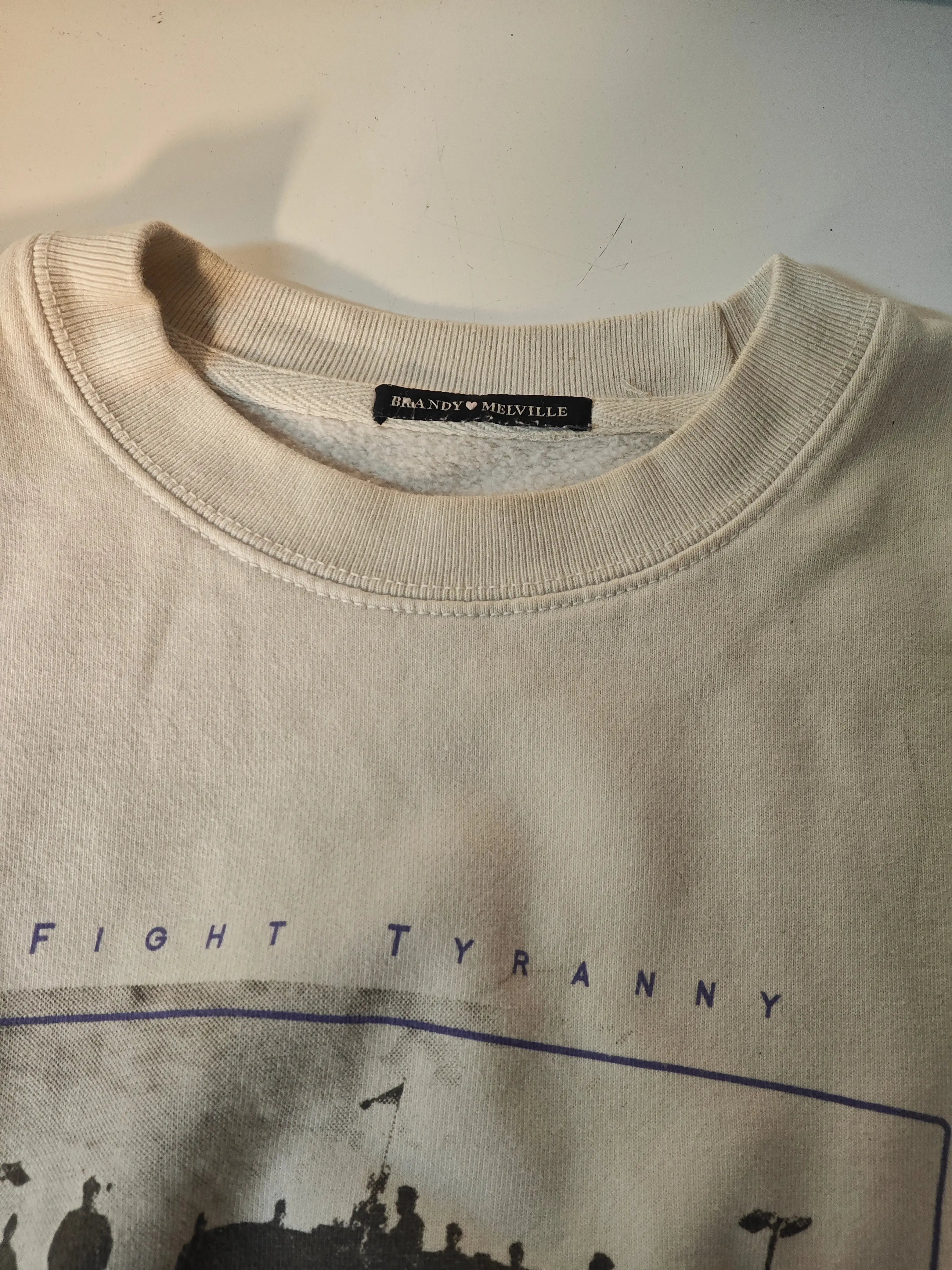 Sweat beige à imprimé, de Brandy Melville, avec un col rond côtelé et l'inscription "Fight Tyranny".
