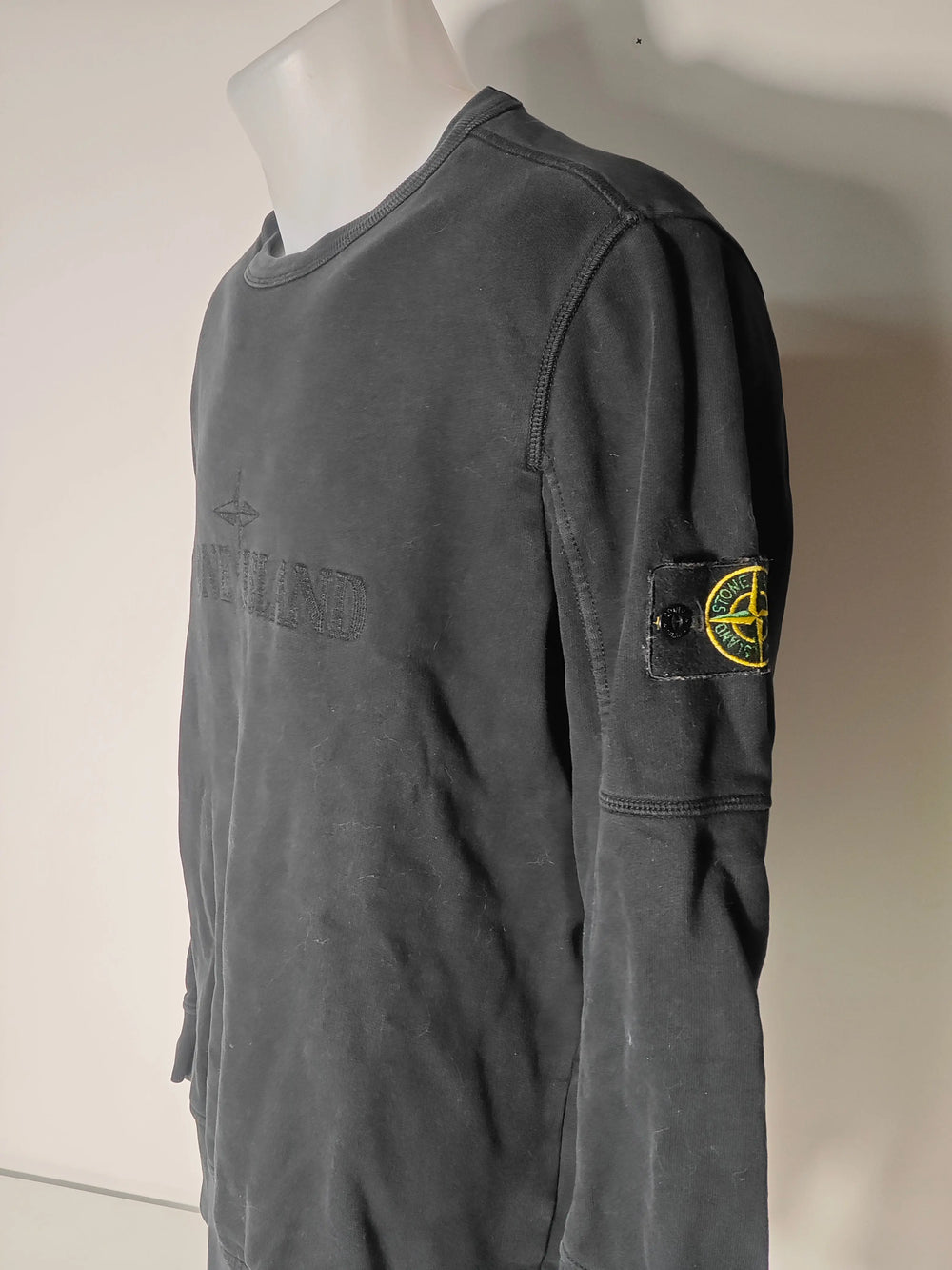 Sweat noir brodé ton-sur-ton de Stone Island, avec écusson logo sur la manche, présenté de côté sur un mannequin.
