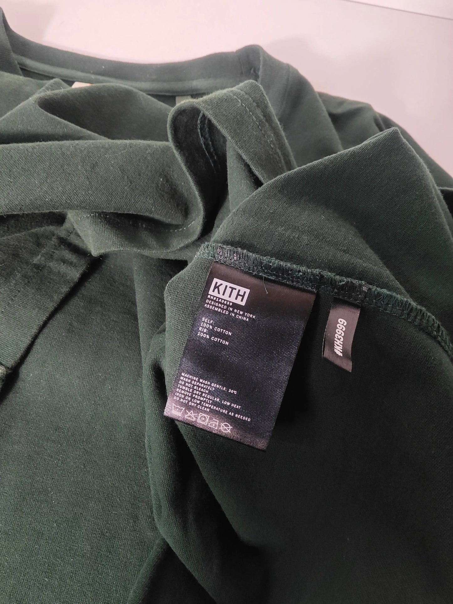 T-shirt vert foncé de Kith avec étiquette d'entretien visible et numéro de modèle.