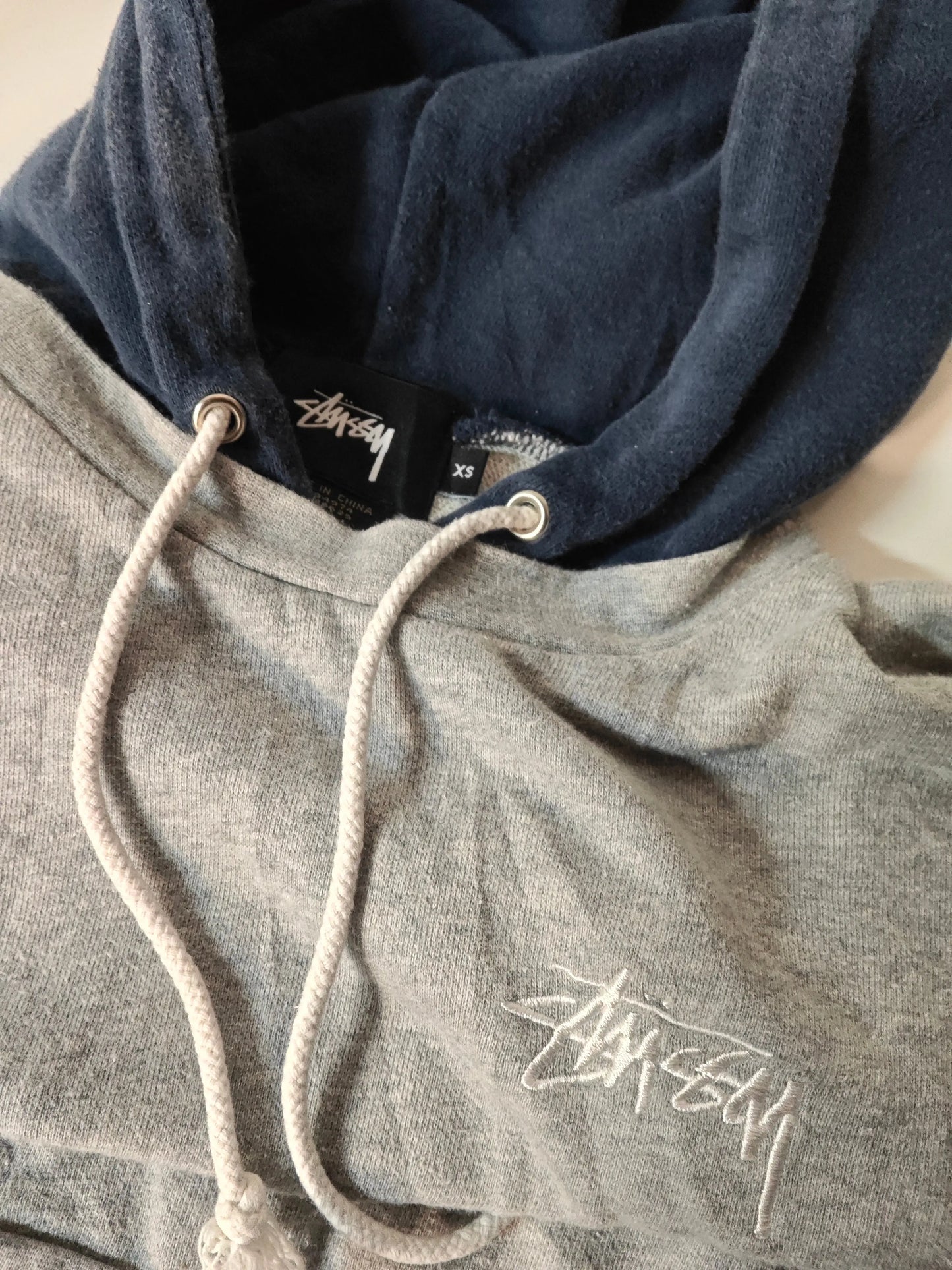Sweat à capuche gris et bleu marine de Stüssy, avec cordon de serrage blanc et logo brodé.