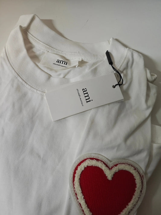 T-shirt blanc en coton AMI Paris avec patch cœur bouclette rouge et détails blancs.
