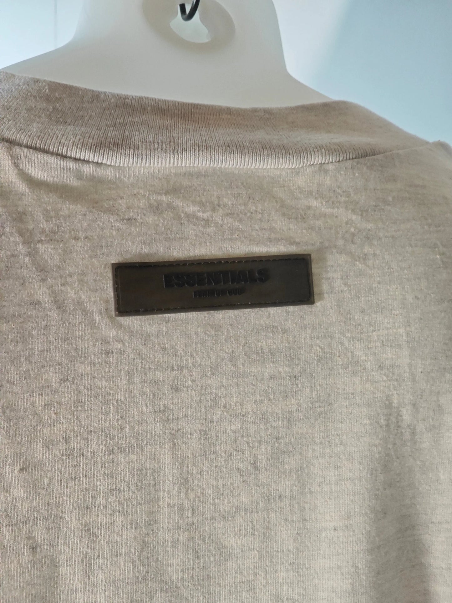 T-shirt beige chiné, de Essentials, avec étiquette logo ton sur ton dans le cou, sur un cintre mannequin.