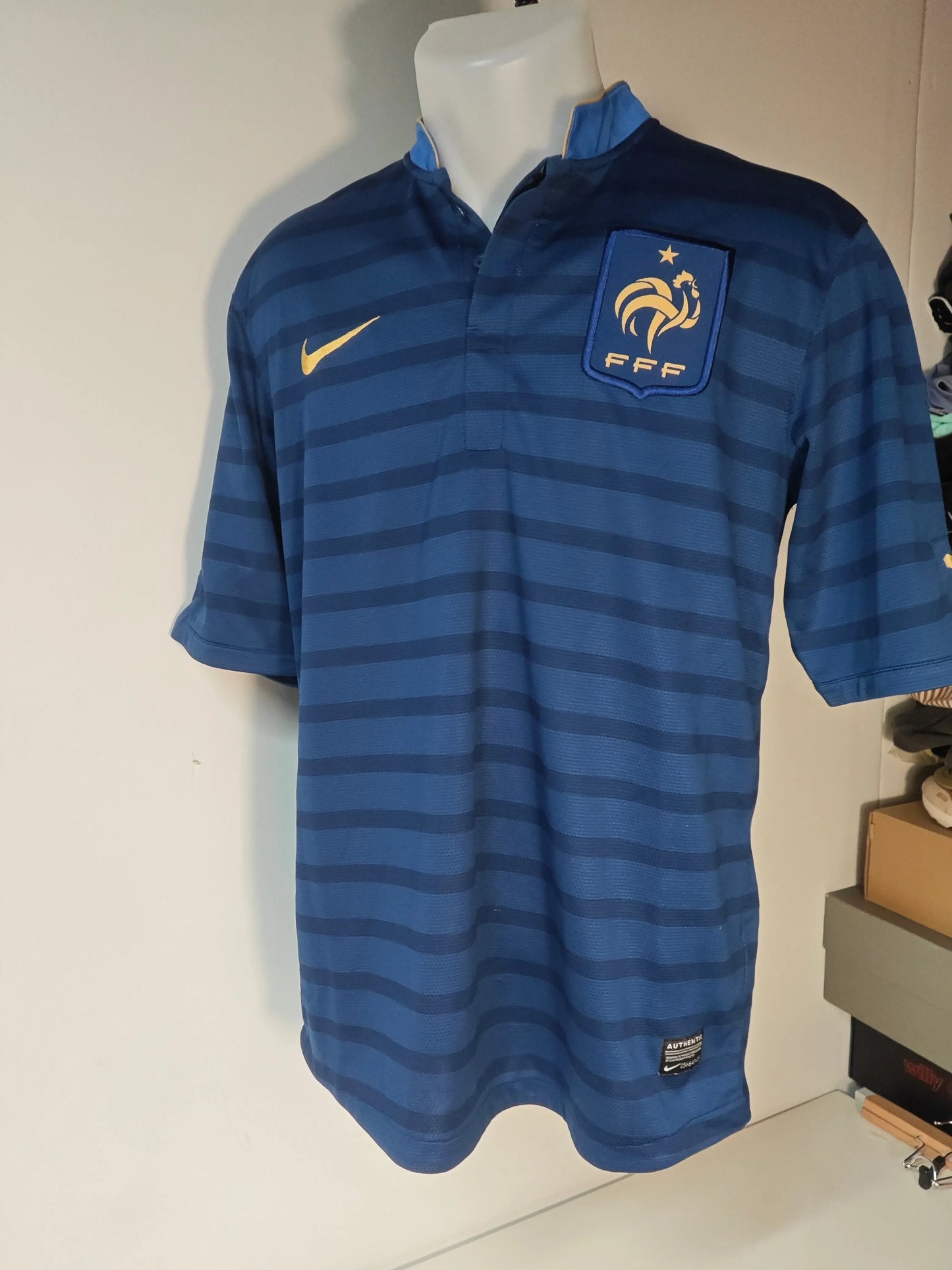 Maillot bleu de l'Équipe de France FFF Dri-Fit par Nike, à rayures horizontales, avec écusson FFF sur la poitrine.
