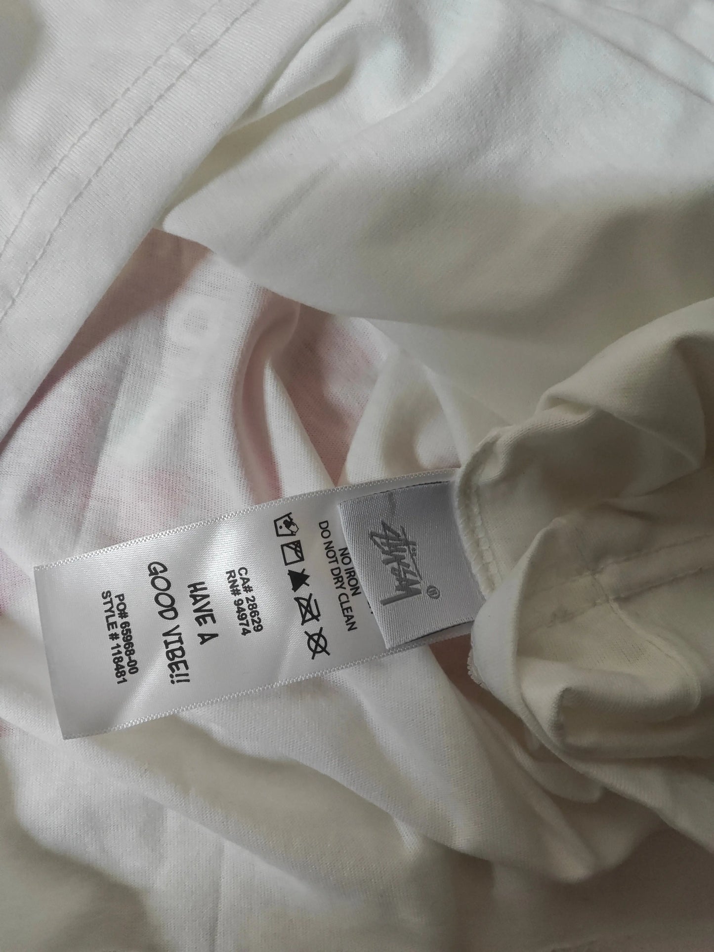 T-shirt blanc, taille L, de Stüssy avec étiquette d'entretien indiquant les instructions de lavage.