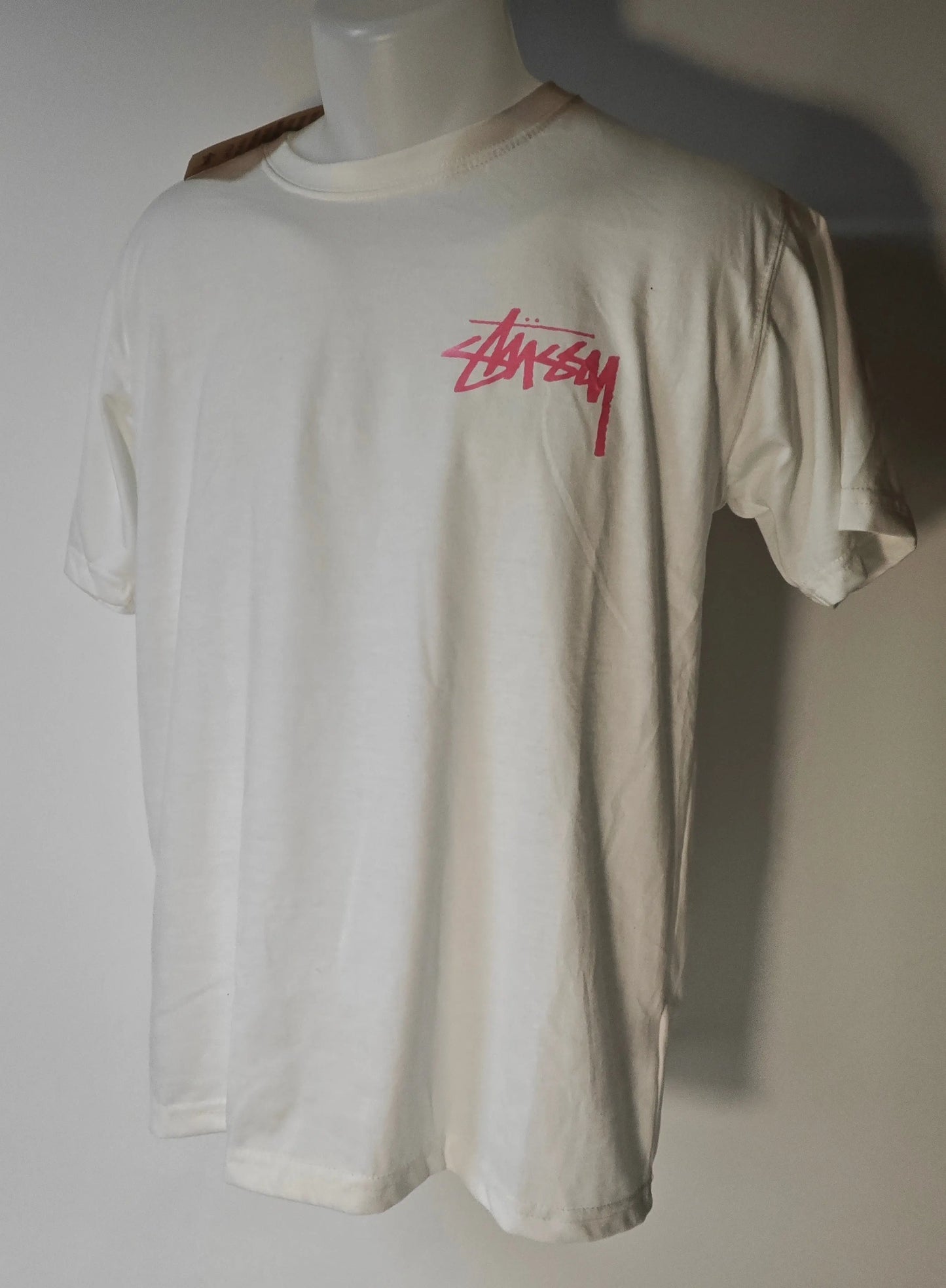 T-shirt blanc taille L de Stüssy avec un logo rose imprimé sur le devant.