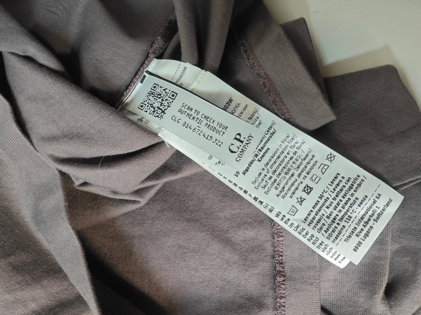 T-shirt taupe en coton, de C.P. Company, avec étiquette d'entretien et QR code apparents.
