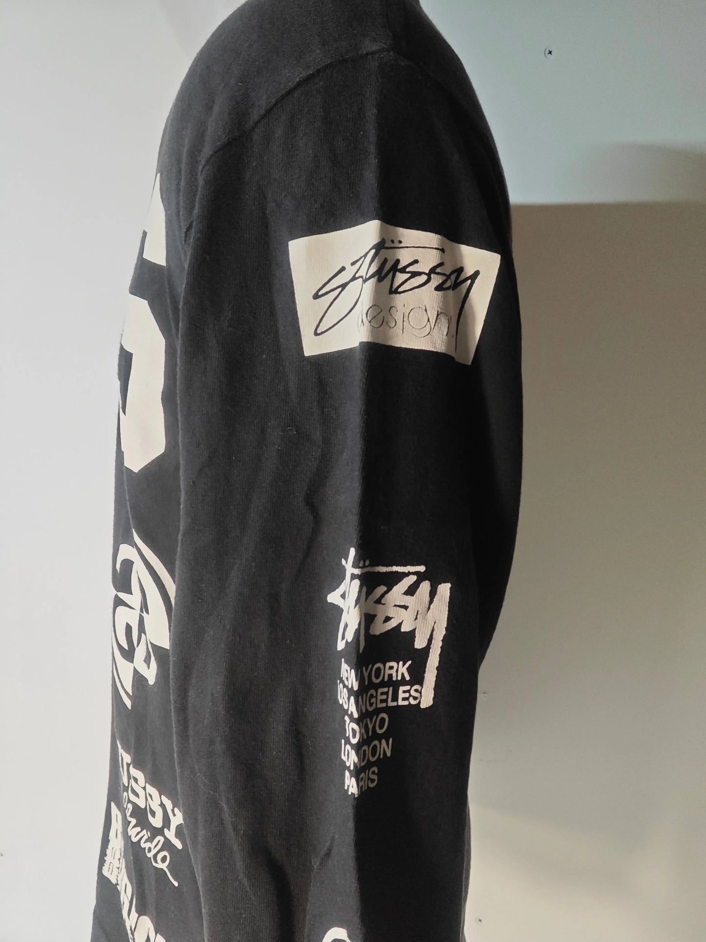 T-shirt noir d'occasion par Stüssy, avec imprimés graphiques blancs de logos et villes emblématiques.