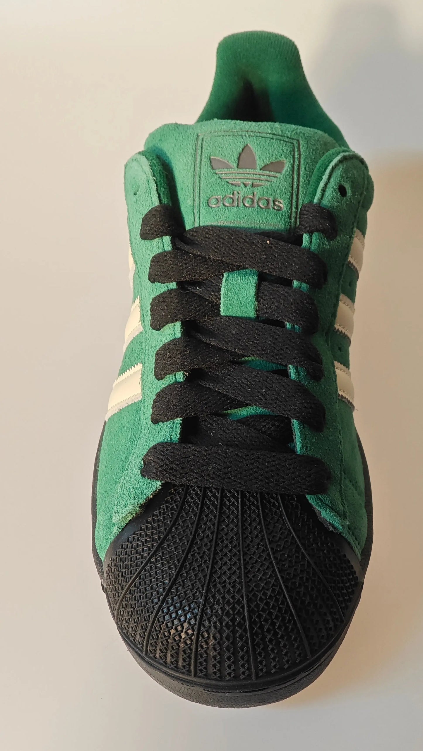 Sneaker verte en daim de Adidas avec des rayures blanches et un bout noir.
