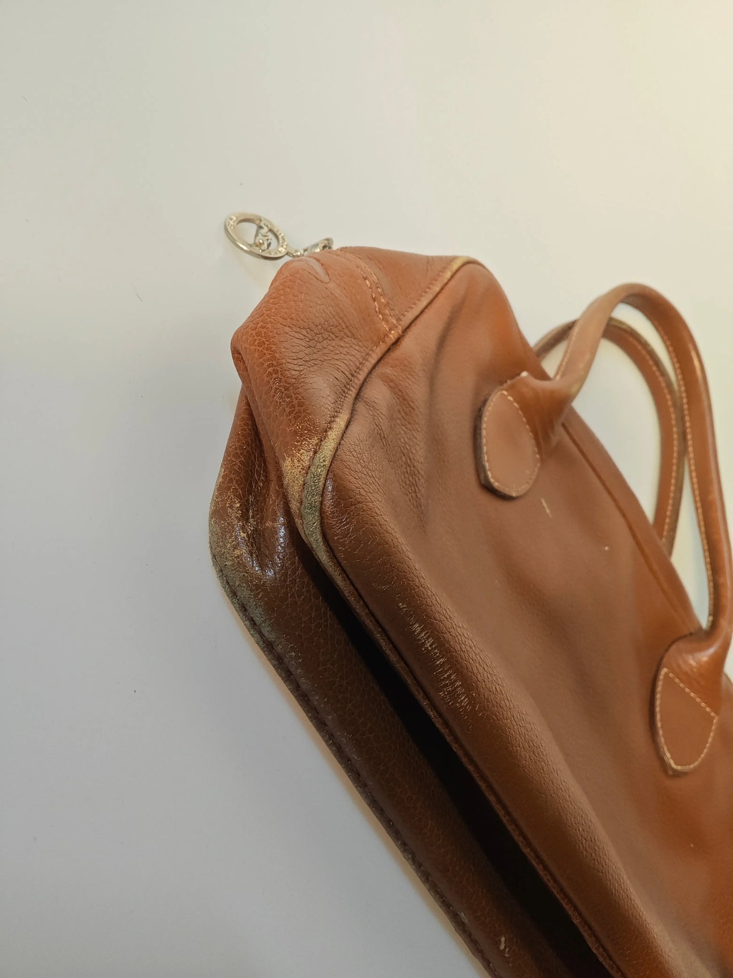 Sac Longchamp en cuir marron authentique de Longchamp, avec poignées arrondies et usure visible sur le côté.