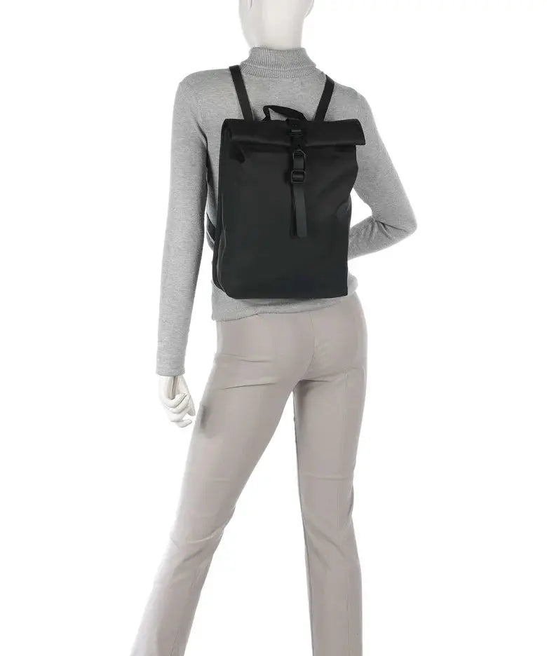 Sac à dos noir de Rains, porté sur le dos d'un mannequin avec un pull gris et un pantalon beige.