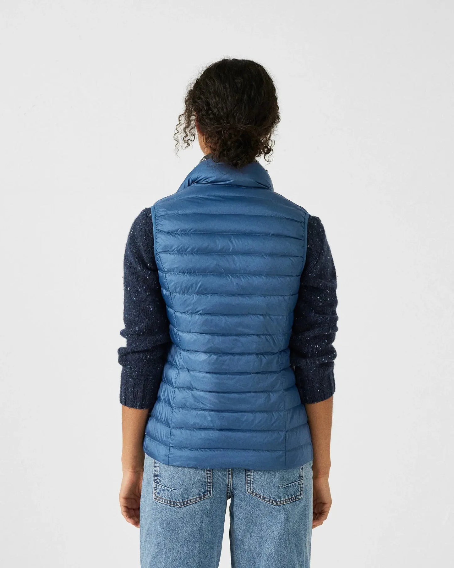 Doudoune sans manches bleue jeans de JOTT, portée avec un pull bleu marine chiné et un jean taille haute.