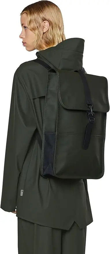 Sac à dos vert grand modèle de Rains, porté avec un manteau imperméable assorti.