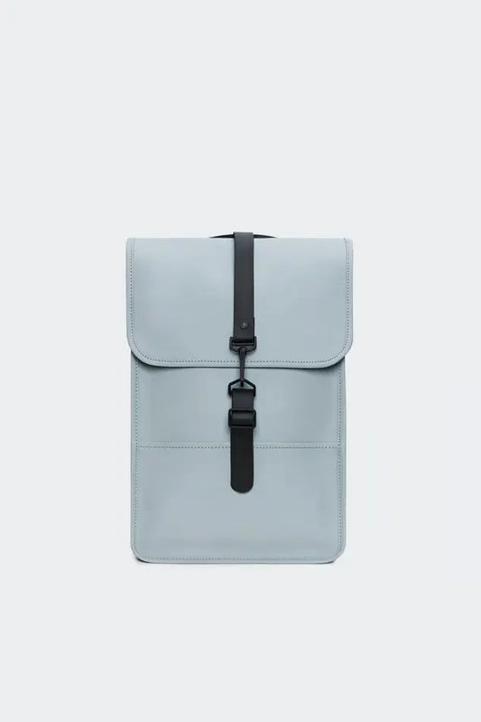 Sac à dos bleu clair par Rains avec une fermeture à sangle noire centrée sur le devant.