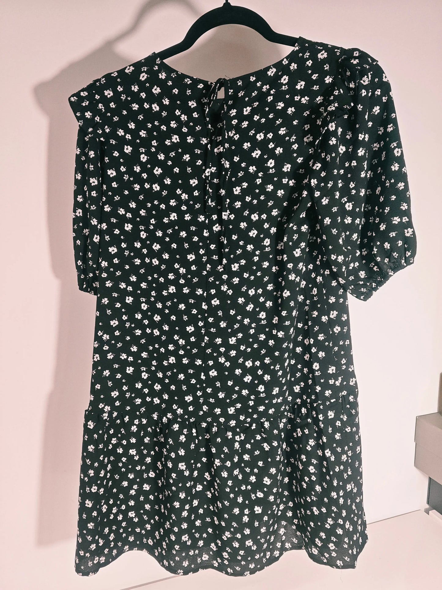 Robe courte fleurie noire, taille XS par H&M, avec motif floral blanc et détail de nœud à l'encolure au dos.