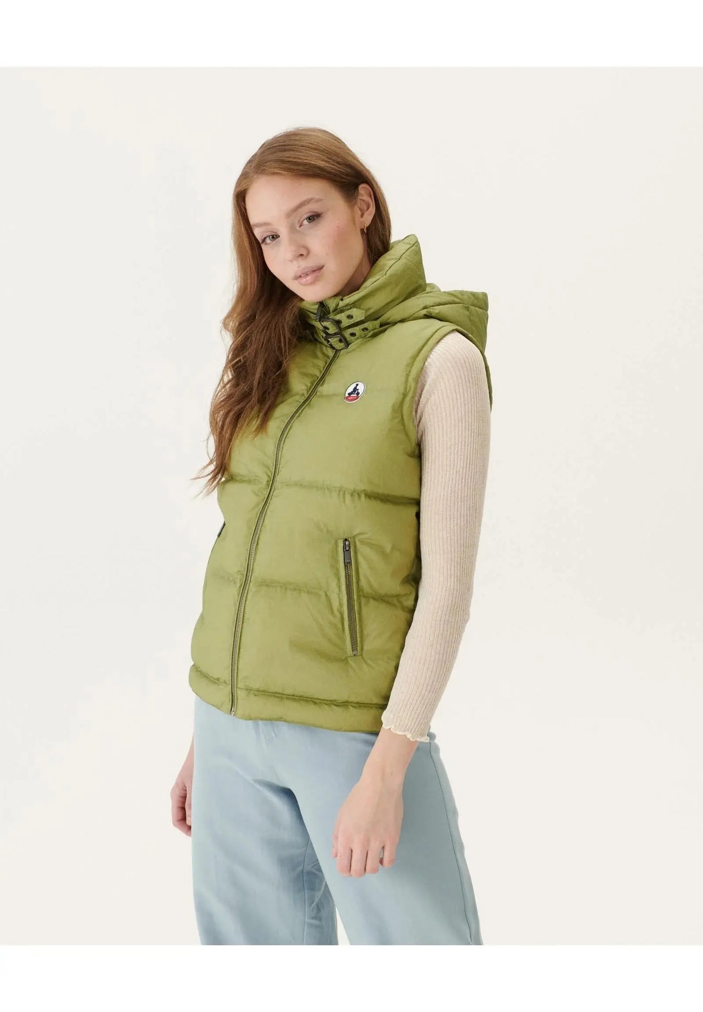 Doudoune sans manches kaki clair de Jott, à capuche et fermeture zippée, portée avec un pull et un pantalon bleu.